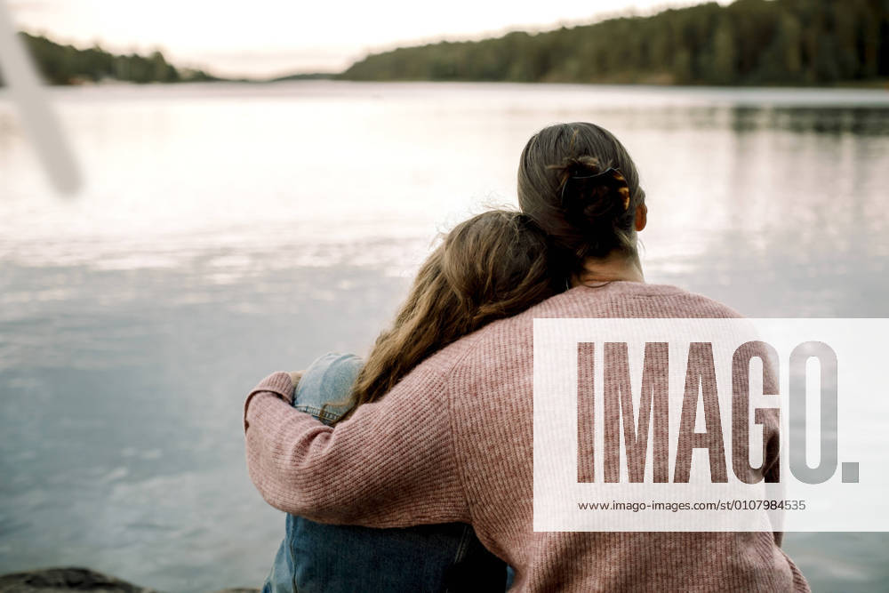 IMAGO Creative, Jahreszeit Sommer, Sommerferien Rear view of mother with daughter sitting by lake, MA82739, Sweden, Stockholm Archipelago, model released