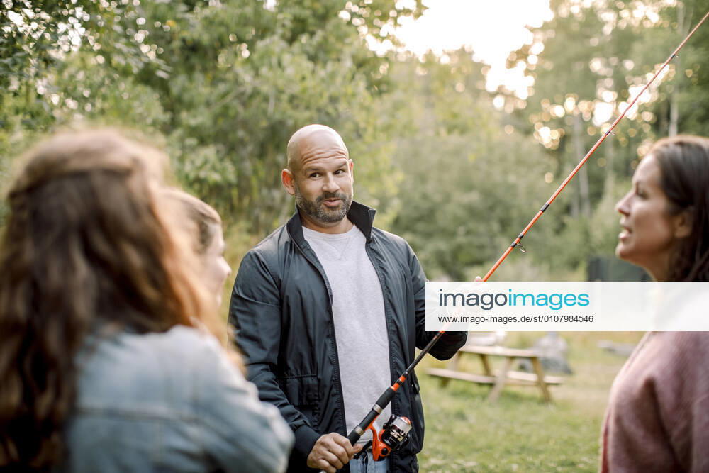 Father with fishing rod talking to daughters while standing by partner in yard, MA82747, Sweden, Stockholm Archipelago, model released