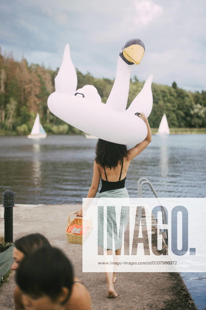 IMAGO Creative, Jahreszeit Sommer, Sommerferien Rear view of teenager carrying inflatable ring overhead while walking towards lake, MA83041, Sweden, Stockholm, model released