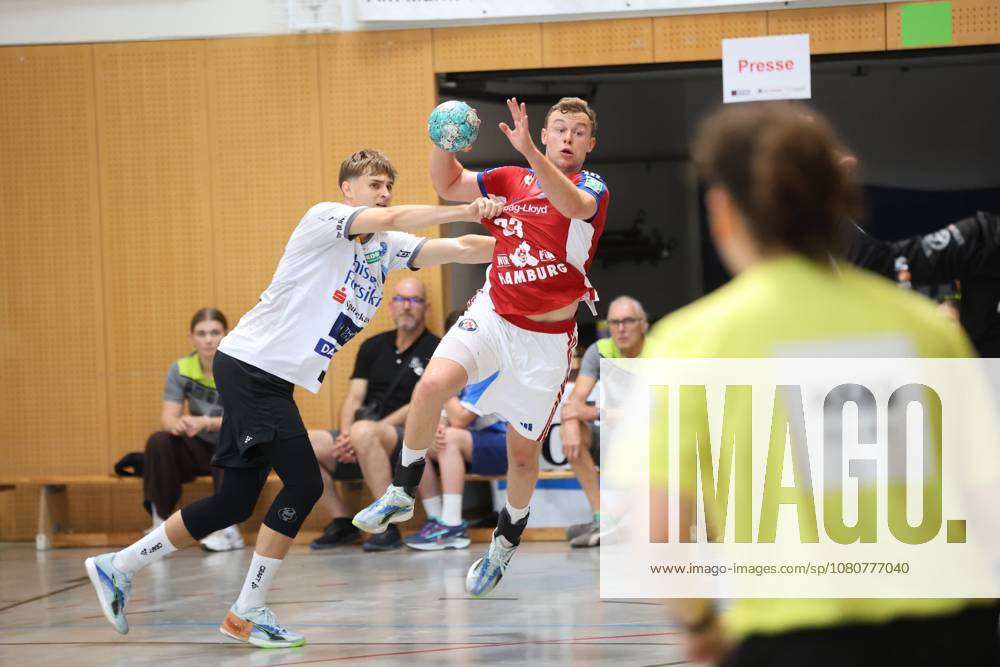 Moritz Sauter, No. 33 of HSV Hamburg, jumps and winds up for a shot, while a player from Mors Thy Handbold tries to block the shot. The ball is clearly visible in the frame; spectators and a referee can be seen in the background. Moritz Sauter, No. 33 of HSV Hamburg, takes a jump shot against Mors Thy Handbold.