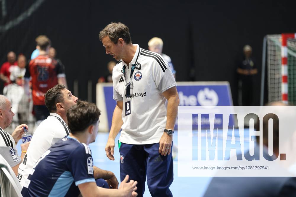 Torsten Jansen, head coach of HSV Hamburg, stands on the sidelines at the Volkswagen Halle in Braunschweig and speaks to the seated players. In the background, players from MTV Braunschweig can be seen. Torsten Jansen of HSV Hamburg gives instructions on the sidelines.