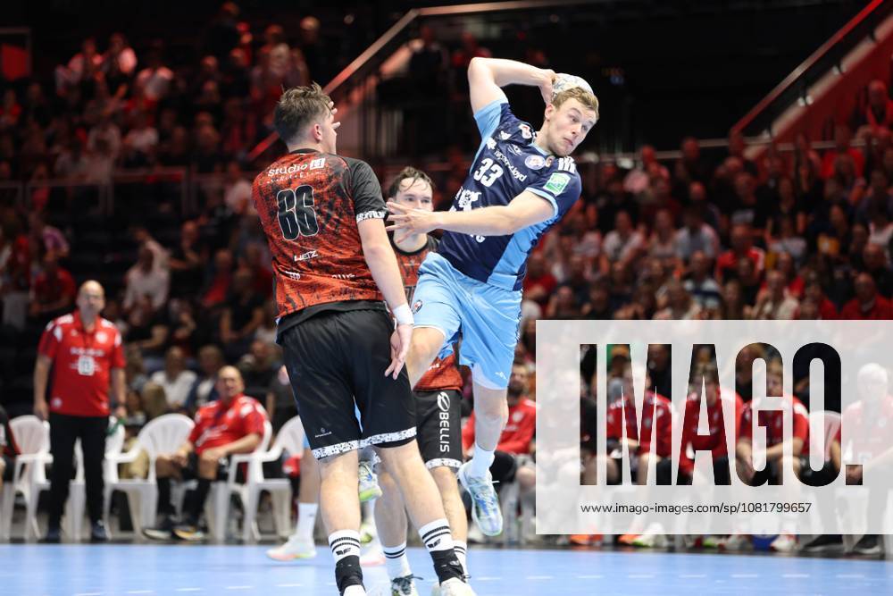 Moritz Sauter, No. 33 of HSV Hamburg, jumps and takes a shot while a player from MTV Braunschweig 86 tries to block the shot. The packed Volkswagen Halle in Braunschweig serves as the backdrop as Moritz Sauter, No. 33 of HSV Hamburg, takes a jump shot against MTV Braunschweig.
