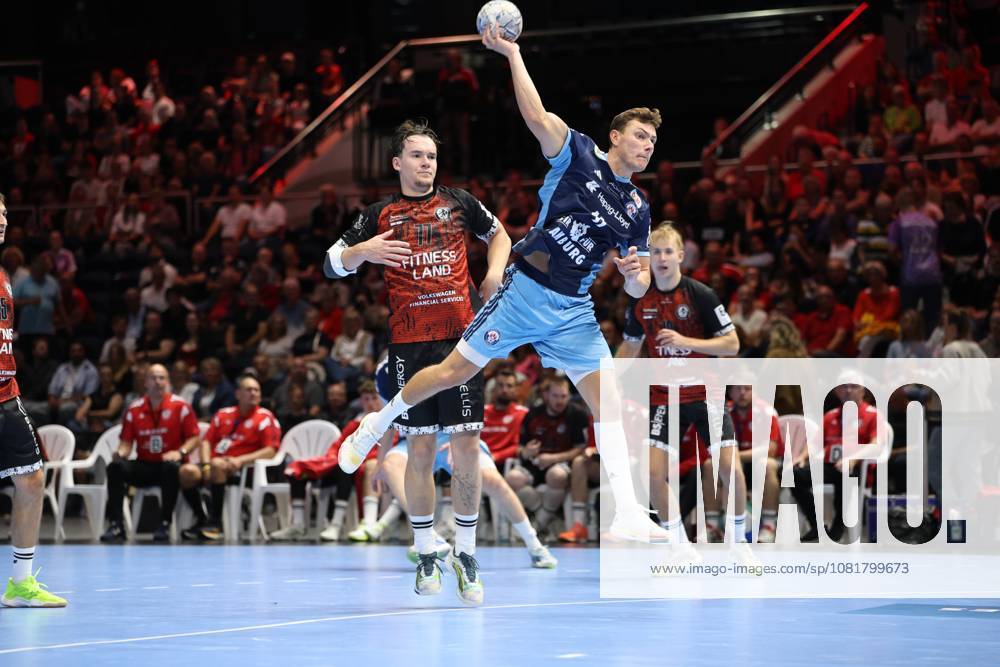 Mika Hoyer 77 of MTV Braunschweig jumps up with the ball in his shooting hand and takes a shot, while an HSV Hamburg player tries to block the shot in a one-on-one battle. The Volkswagen Halle in Braunschweig is packed with spectators. Mika Hoyer 77 of MTV Braunschweig takes a jump shot against HSV Hamburg.