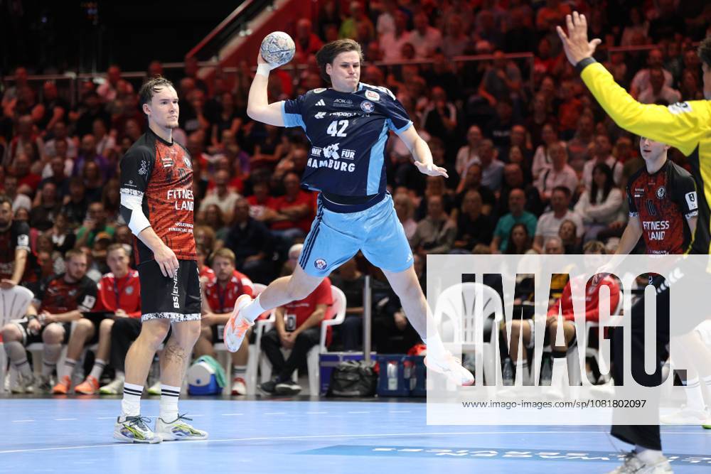 Jan Christian Schmidt, 42, of HSV Hamburg jumps and prepares to shoot; the ball is already above his head. Mika Hoyer, 77, of MTV Braunschweig watches the action from behind as the MTV goalkeeper raises his arm. Jan Christian Schmidt, 42, of HSV Hamburg takes a jump shot against MTV Braunschweig.