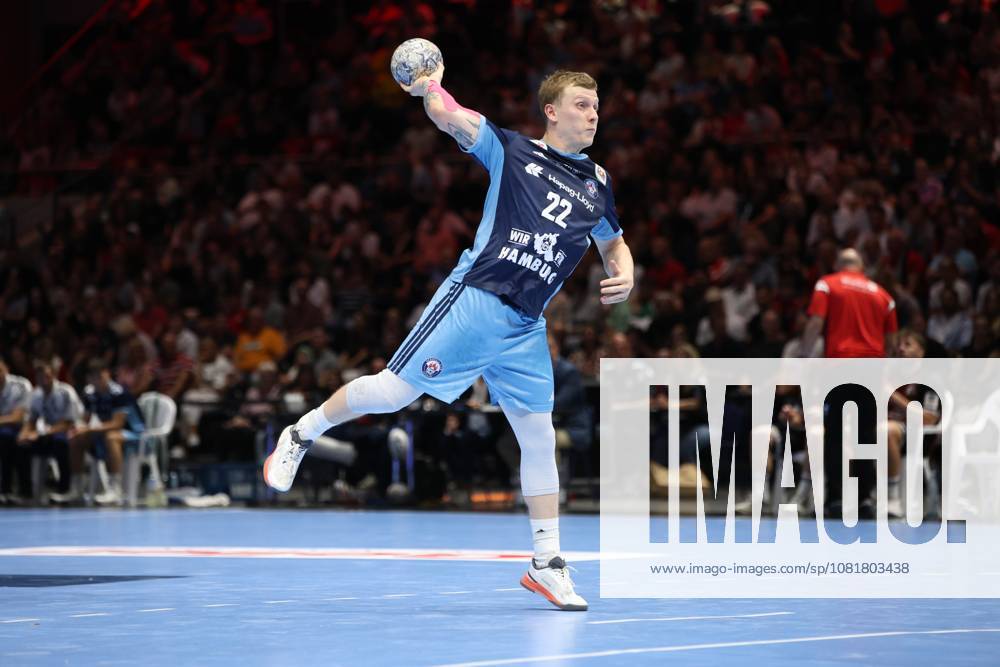 Noah Beyer, 22, of HSV Hamburg takes a shot at the Volkswagen Halle in Braunschweig and holds the ball aloft with his arm outstretched. The left wing can be seen in the middle of his shot, with one leg raised, with a well-filled spectator stand in the background. Noah Beyer, 22, of HSV Hamburg, taking a shot at the Volkswagen Halle
