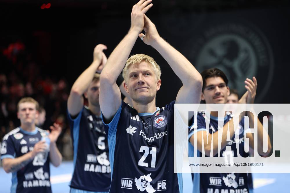 Frederik Bo Andersen, No. 21 of HSV Hamburg, claps his hands with his arms raised and celebrates with his teammates, including Kaj Geenen, 17, of HSV Hamburg, celebrating the victory at the Volkswagen Halle in Braunschweig. The entire HSV Hamburg team applauds together toward the fans. Frederik Bo Andersen, 21, of HSV Hamburg, and Kaj Geenen, 17, of HSV Hamburg, celebrate.