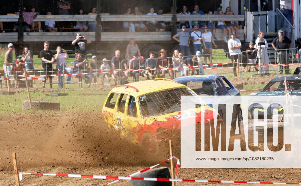 Several stock cars are locked in a close battle during the FUN CROSS stock car race near Dietenwengen. The yellow-and-red car in the foreground kicks up large amounts of dirt as it speeds through the curve. Numerous spectators watch the race in the background. FUN CROSS stock car race in Eberhardzell Eberhardzell Dietenwengen