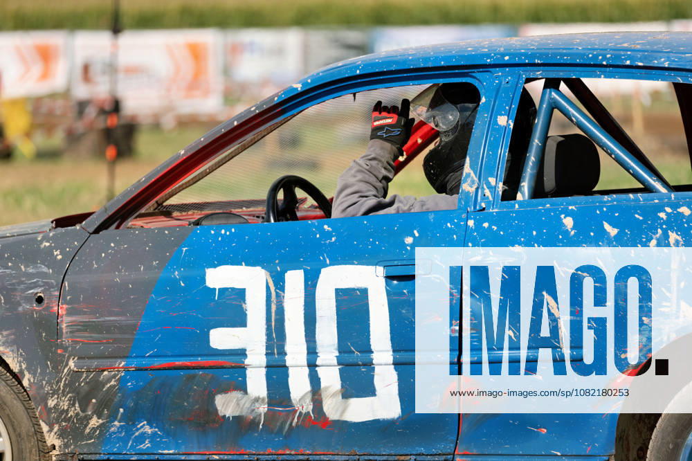 The driver of the blue stock car with start number 310 raises his hand during the FUN CROSS stock car race near Dietenwengen. The vehicle is clearly covered in mud, scratches, and marks from the race laps FUN CROSS stock car race in Eberhardzell Eberhardzell Dietenwengen