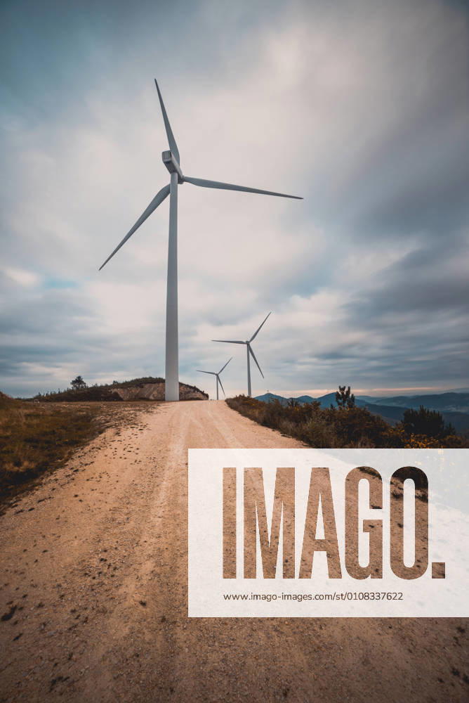 IMAGO Creative: Klimawandel - Zukunft und Innovation Row of modern windmills standing on side of narrow countryside road on cloudy day