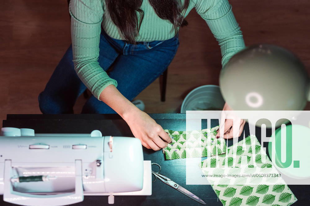 Cropped unrecognizable female tailor sitting in table making face masks near modern sewing machine in loft style atelier, Model released, Property released