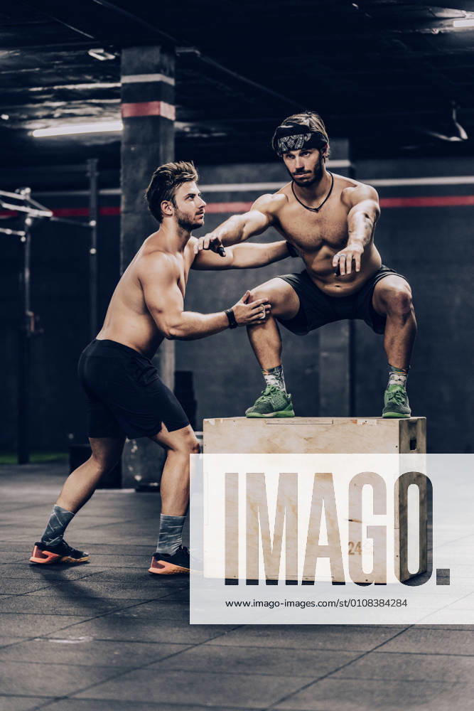 IMAGO Kreativ: Bildung, Sporterziehung Athletic trainer jumping on box and helping client to improve stamina in gym, Model released, Property released