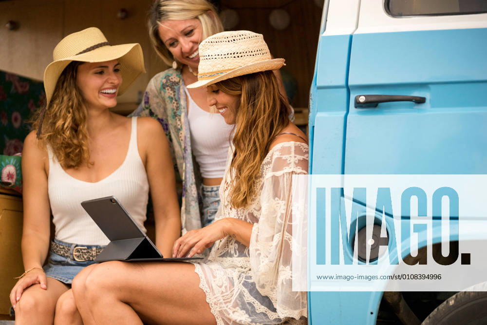 Charming long haired woman in beach wear browsing tablet and talking with smile sitting in car salon