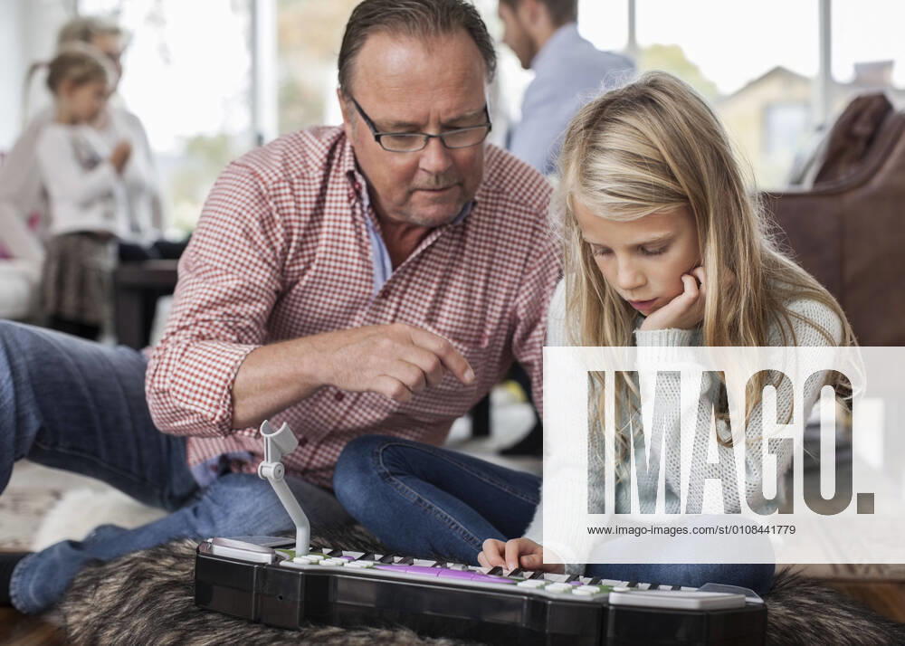 IMAGO Creative: Bildung, Musikerziehung Grandfather and granddaughter playing piano with family in background at home , model released