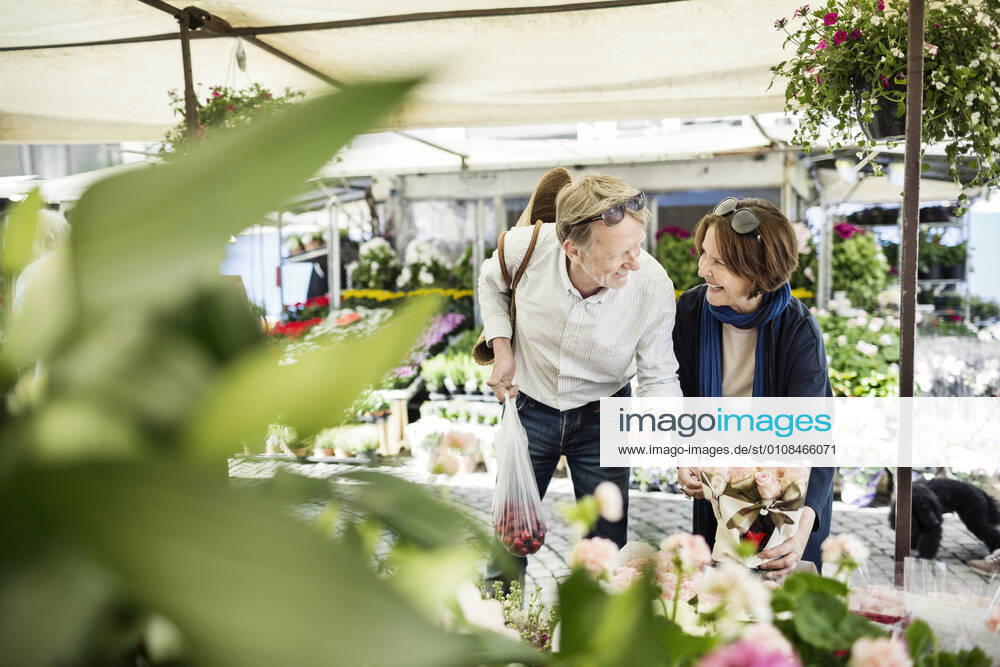 Happy senior couple talking while buying flowers at market , model released