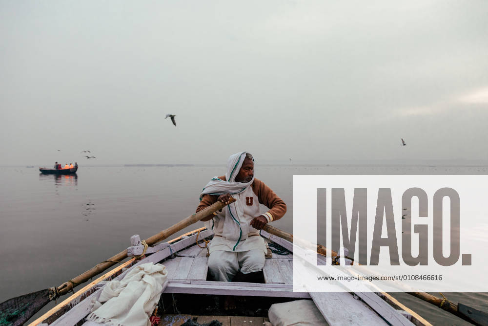 Varanasi, India - February, 2018: Indian male in white clothes sitting in boat and rowing over river