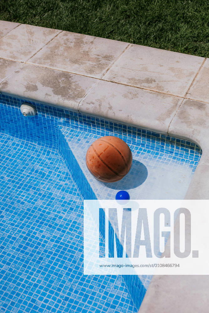 From above of basketball ball in corner on swimming pool in terrace of house with green grass
