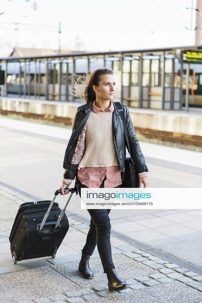 Full length of businesswoman pulling wheeled luggage while walking on railroad station platform , model released