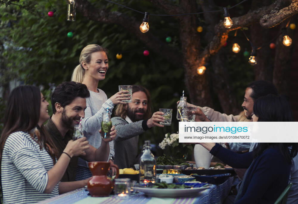 Multi-ethnic friends toasting drinks at dinner table in yard , model released