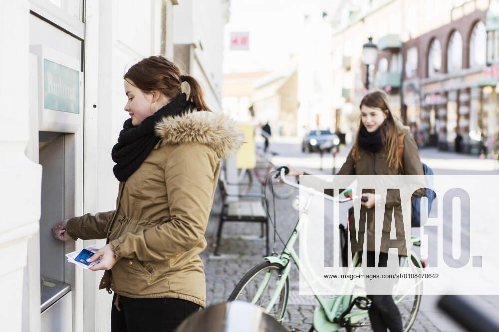Young woman at cash machine with female friend in background , model released