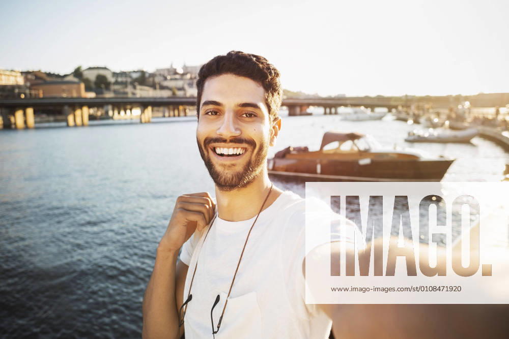 IMAGO Creative, Jahreszeit Sommer, Sommer in der Stadt Portrait of happy male tourist by river in city , model released