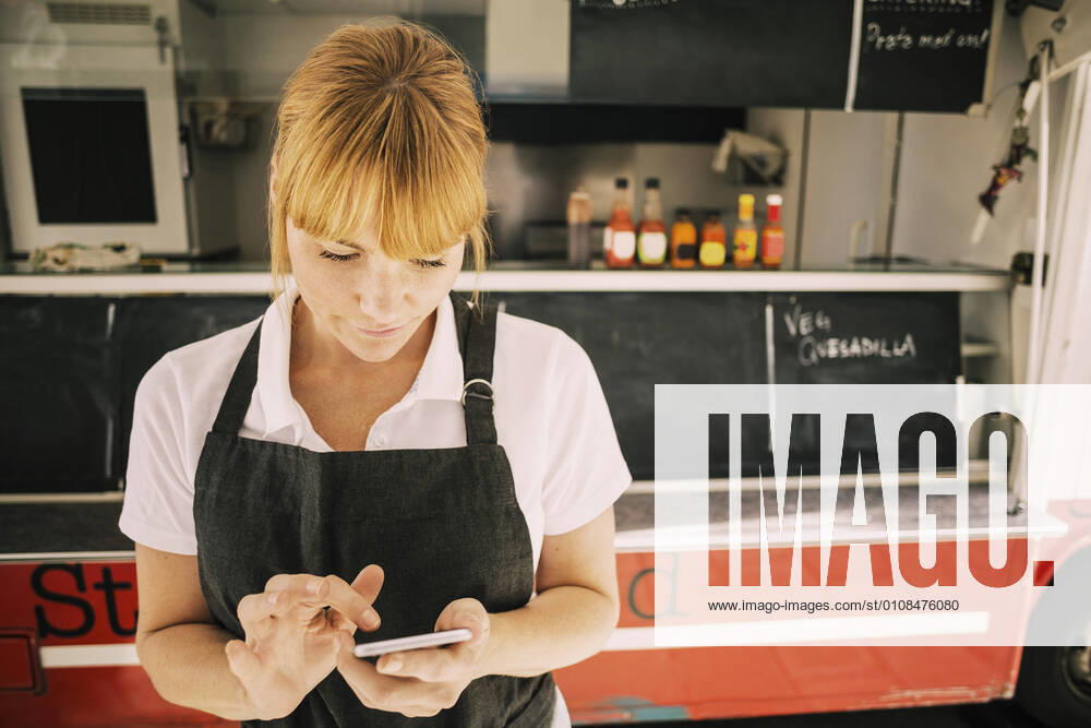 Close-up of female chef using mobile phone against food truck , model released