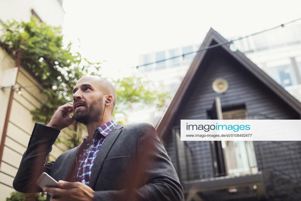 Low angle view of businessman talking through in-ear headphones at office yard , model released, property released
