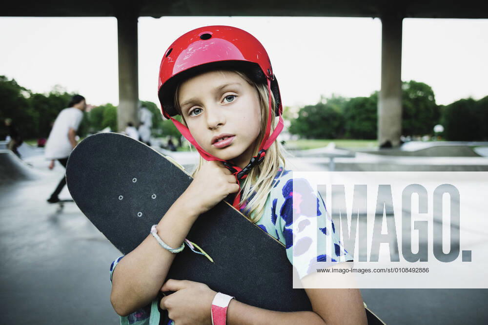 Portrait of girl wearing red helmet holding skateboard at park , model released