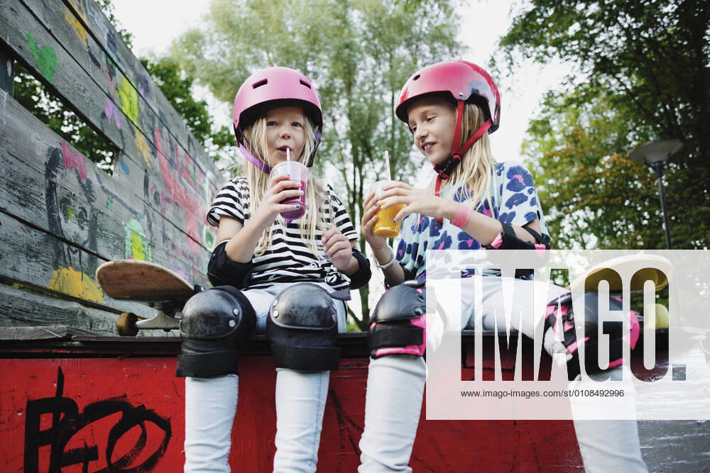 Smiling friends enjoying drink while sitting on edge of skateboard ramp , model released