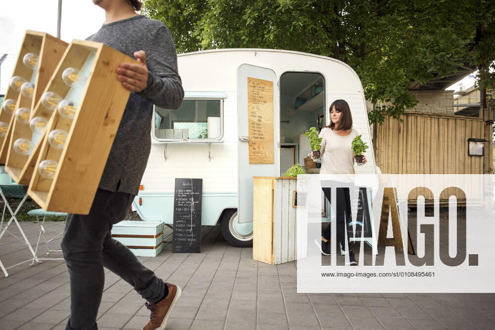 Owners carrying letter M and potted plants while walking outside food truck on street , model released, property released