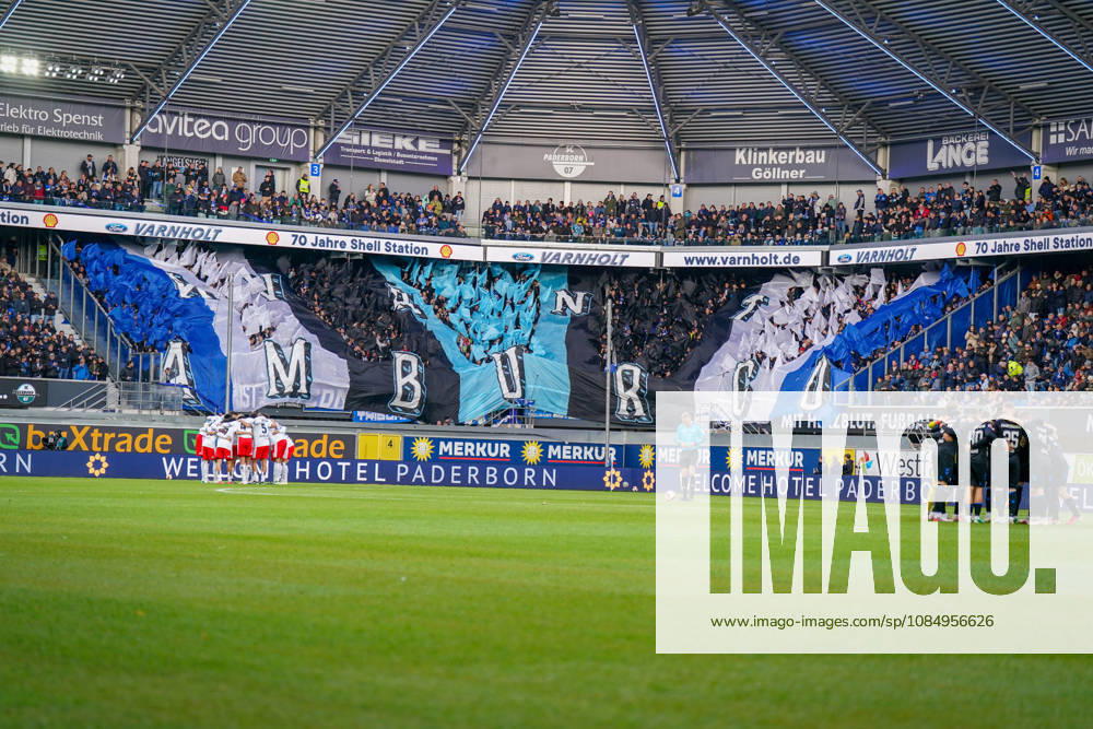 Germany Soccer Bundesliga 2026–2027, Matchday 7: SC Paderborn vs. Hamburger SV at Home Deluxe Arena, Paderborn. Interior view of the Home Deluxe Arena in Paderborn featuring a large blue, black, and white choreographed display by the home fans of SC Paderborn 07, with HAMBURG lettering. Fans, Ultras, fan choreography, fan scene, flags, spectators, stands, fan section, atmosphere, pre-match team circles for SC Paderborn and Hamburger SV, soccer, Bundesliga, stadium, sports venue, wide shot, playing field, referee, floodlights, advertising, sponsors, advertising banners, Merkur, buXtrade, Varnholt, Welcome Hotel