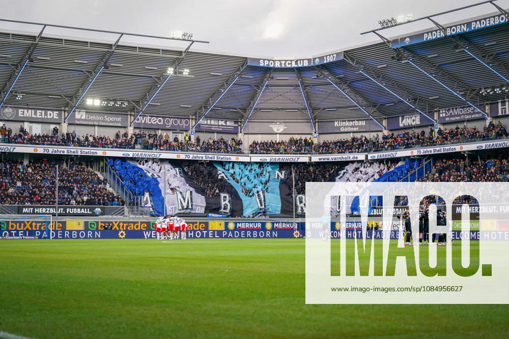 Germany Soccer Bundesliga 2026–2027, Matchday 7: SC Paderborn vs. Hamburger SV at Home Deluxe Arena, Paderborn. Interior view of the Home Deluxe Arena in Paderborn featuring a large blue, black, and white choreographed display by the home fans of SC Paderborn 07, with HAMBURG lettering. Fans, Ultras, fan choreography, fan scene, flags, spectators, stands, fan section, atmosphere, pre-match team circles for SC Paderborn and Hamburger SV, soccer, Bundesliga, stadium, sports venue, wide shot, playing field, referee, floodlights, advertising, sponsors, advertising banners, Merkur, buXtrade, Varnholt, Welcome Hotel