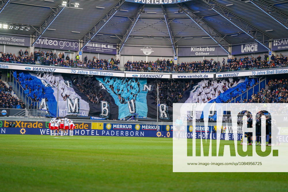 Germany Soccer Bundesliga 2026–2027, Matchday 7: SC Paderborn vs. Hamburger SV at Home Deluxe Arena, Paderborn. Interior view of the Home Deluxe Arena in Paderborn featuring a large blue, black, and white choreographed display by the home fans of SC Paderborn 07, with HAMBURG lettering. Fans, ultras, fan choreography, fan scene, flags, spectators, stands, fan section, atmosphere, pre-match team circles for SC Paderborn and Hamburger SV, soccer, Bundesliga, stadium, sports venue, wide shot, playing field, referee, floodlights, advertising, sponsors, advertising banners, Merkur, buXtrade, Varnholt, Welcome Hotel