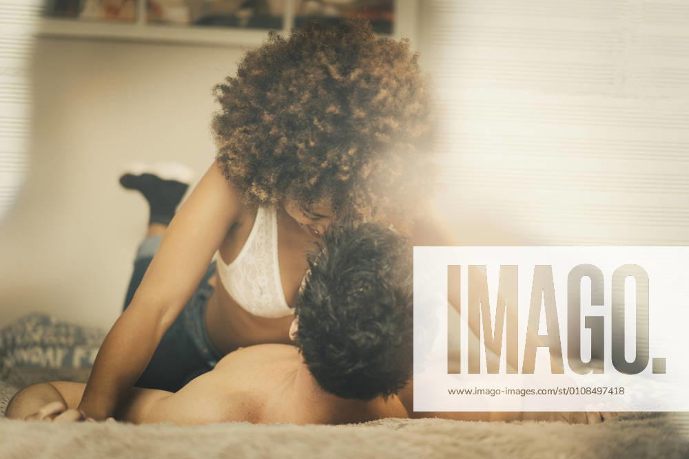 Young diverse man and woman lying on bed and cuddling in cozy room at home, Model released