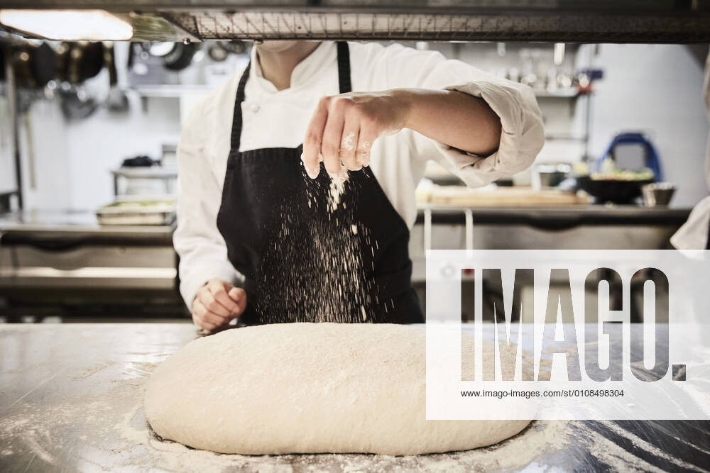 Midsection of female chef student sprinkling flour on dough at commercial kitchen , model released, property released