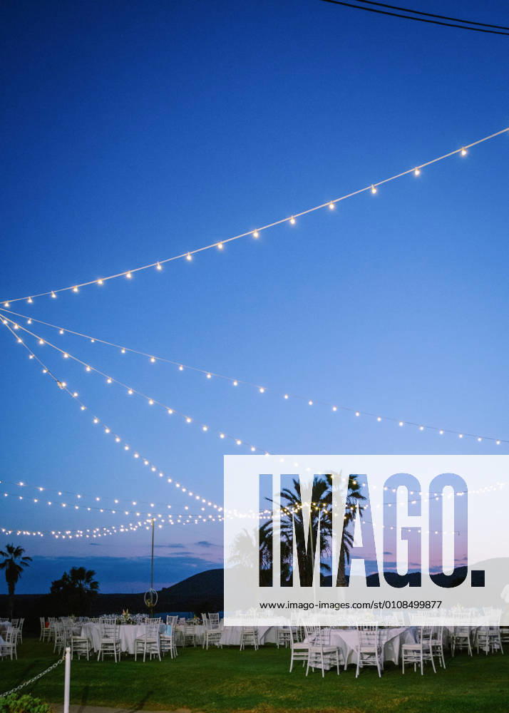 Glowing garlands hanging over banquet tables and chairs prepared for wedding party in evening