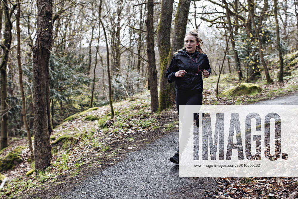 Full length determined female athlete running on narrow road in forest , model released