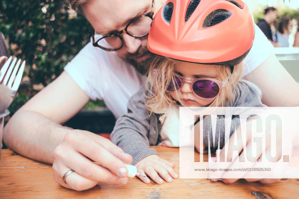 IMAGO Creative, Urban Lifestyle Father painting daughter s nails at table outdoors , model released