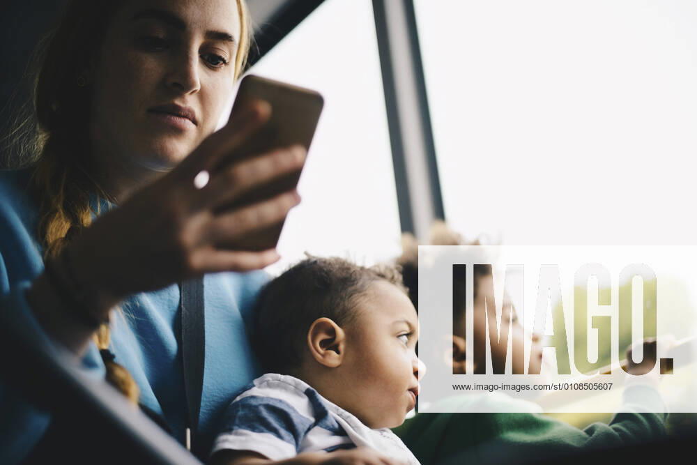 Mother using mobile phone while sitting with son in bus , model released