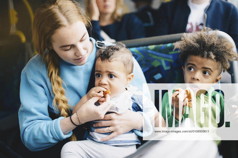 IMAGO Creative: Gesellschaft, Mobilität auf dem Land IMAGO Creative: Stadt-Dichotomien Mother feeding baby boy while sitting with son in bus , model released