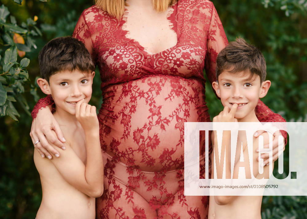 Pregnant woman hugging twin boys in garden, Model released