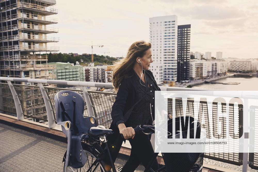 IMAGO Creative: Business, Innovative Technologie-Lösungen Mature woman walking with bicycle on footbridge in city , model released