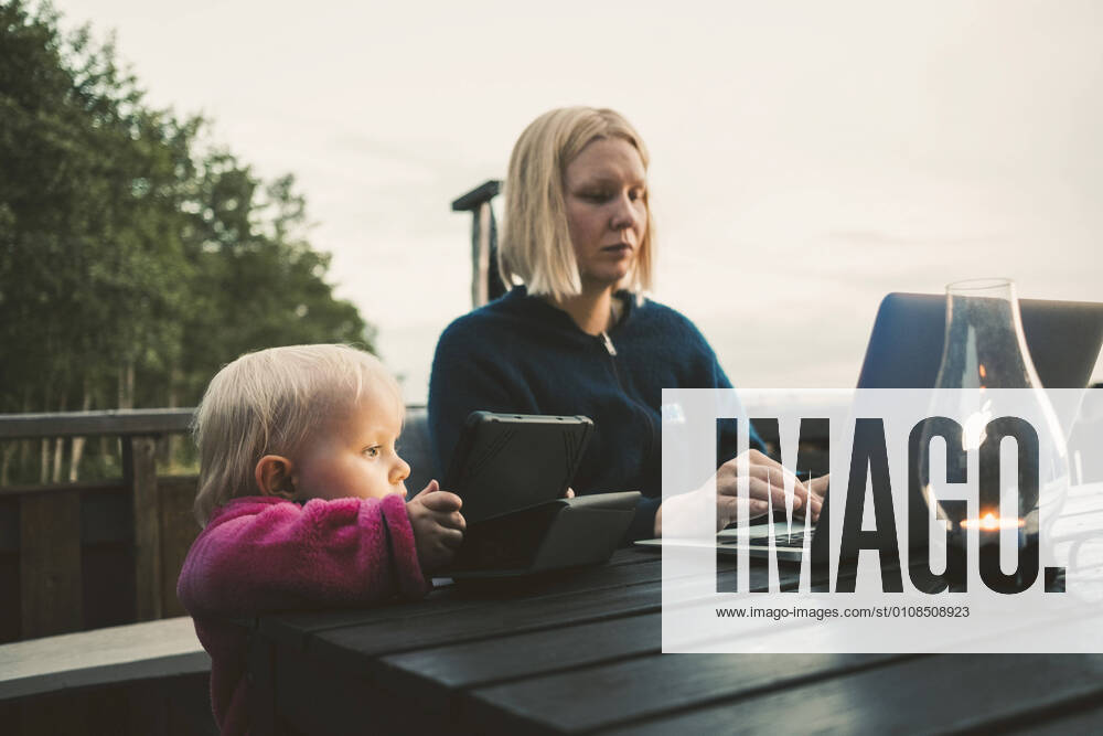 Daughter holding digital tablet while mother using laptop at table against sky , model released, property released