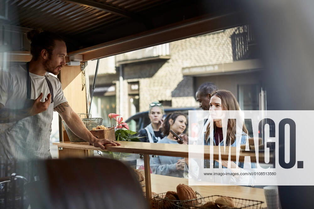 Young male owner taking order from female customer at food truck in city , model released, property released