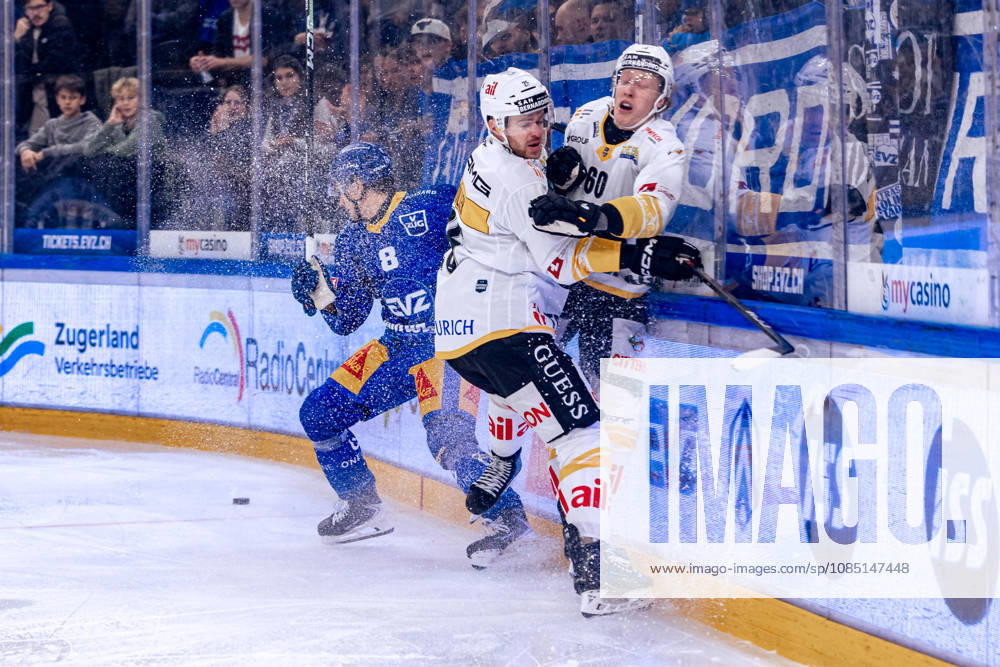 Rico Gredig 8 (EV Zug) evades a check by Mirco Müller 25 (HC Lugano); instead, Lassi Thomson 60 (HC Lugano) is hit. 27 10 2026 National League, Regular Season, Ice Hockey, OYM Hall, EV Zug vs. HC Lugano. Photo by