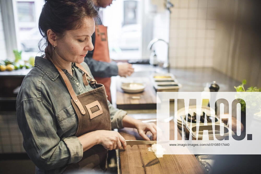 IMAGO Creative: Landleben - Essen Mature female chef cutting food on board at counter in restaurant kitchen , model released, property released