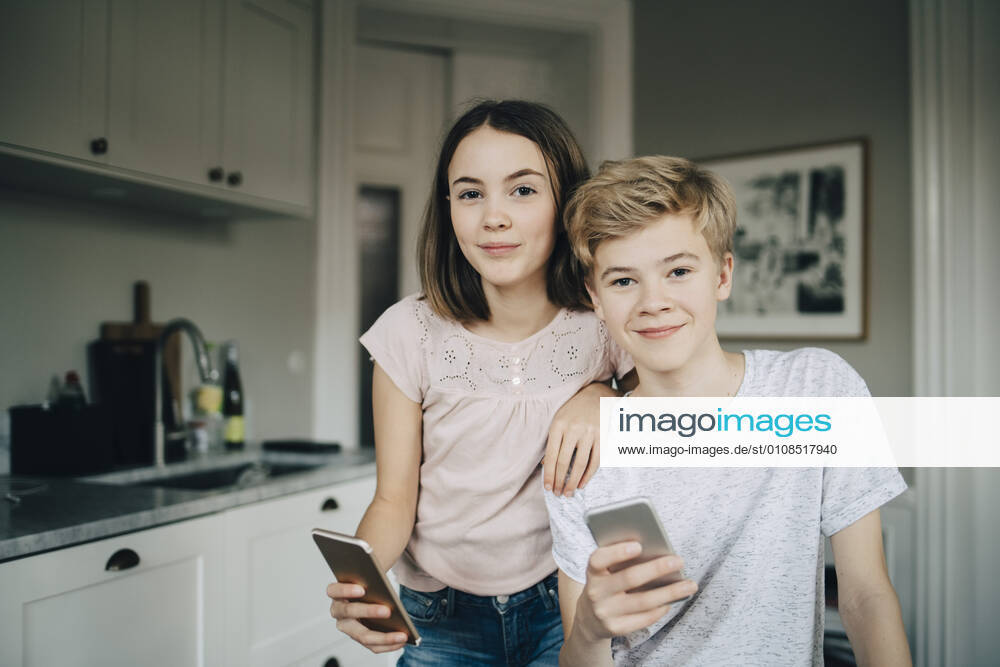 Portrait of smiling male and female friends holding smart phones at home , model released, property released