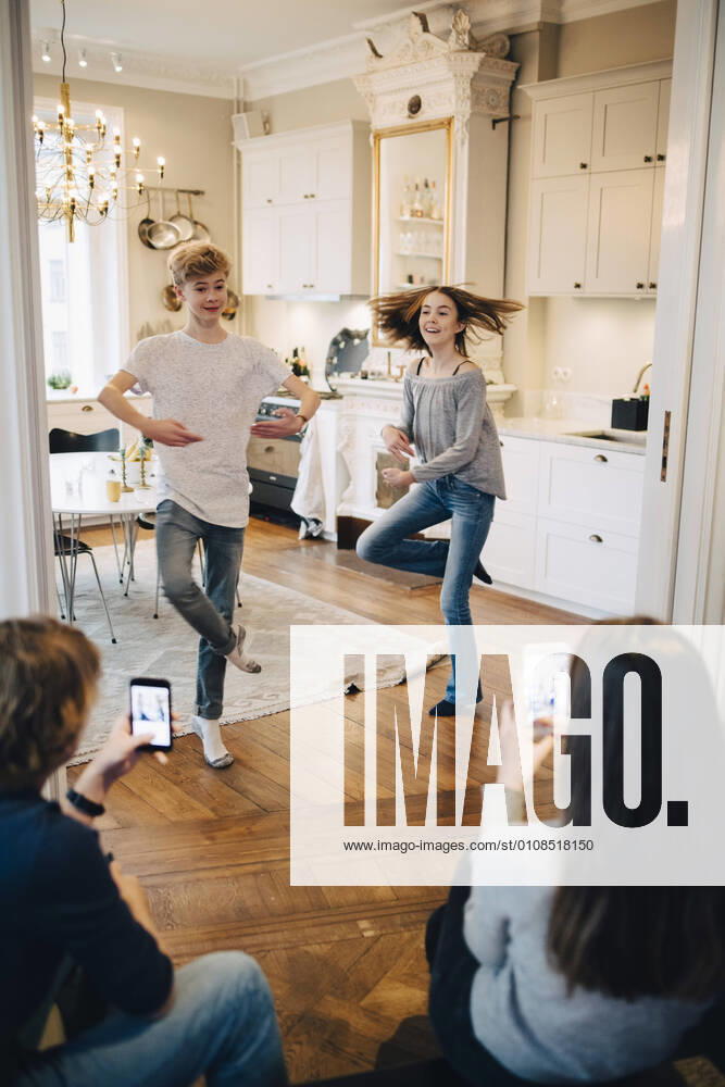 Friends photographing teenage boy and girl dancing at home , model released, property released