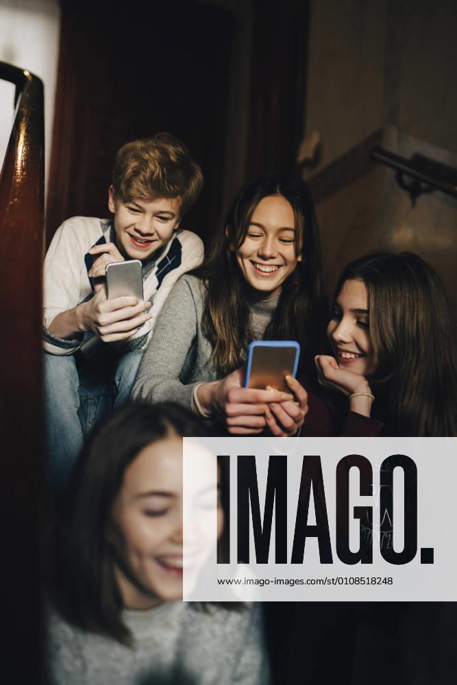 Happy teenage boy with female friends using mobile phone while sitting on steps , model released