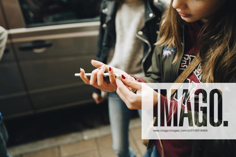 Midsection of girl connecting cable to mobile phone while walking with friends , model released