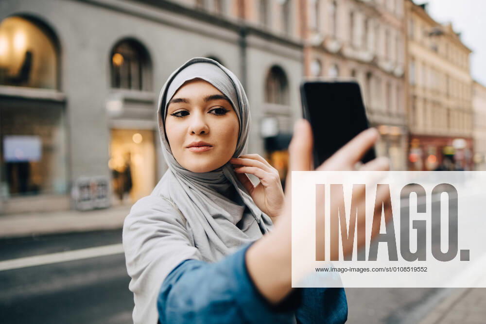 Confident young Muslim woman taking selfie on city street , model released